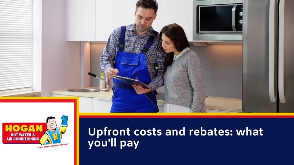 A technician in overalls reviewing a hot water installation paperwork on a clipboard with a homeowner in a kitchen