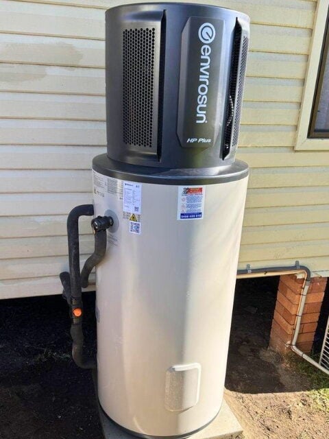 An Envirosun heat pump hot water system unit with Smart Home tech installed outside against house siding.