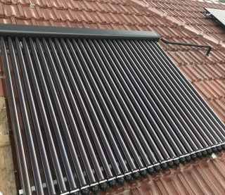 An evacuated tube solar collector panel installed on a brown tiled roof