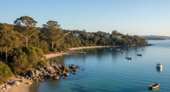 An elevated, wide view of a calm turquoise bay curving along a sandy beach and a rocky shoreline.