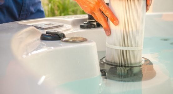 A close-up view of a person's hands installing or removing a cylindrical, pleated white cartridge filter.