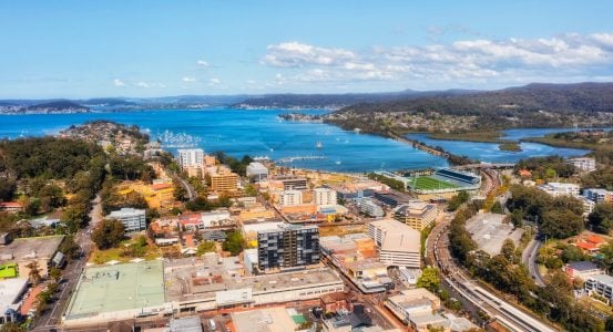 Hot Water Installation and Maintenance North Gosford A coastal city with mid-rise buildings, a sports stadium, and a railway line running along the shore.