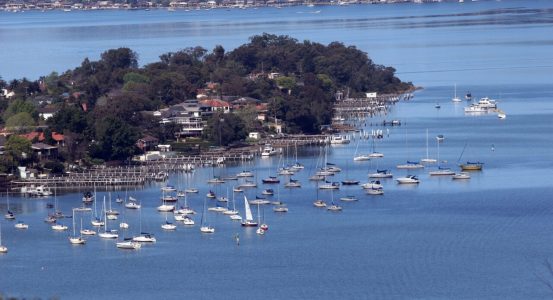 A calm blue bay filled with numerous anchored sailboats and small motorboats in Point Frederick.
