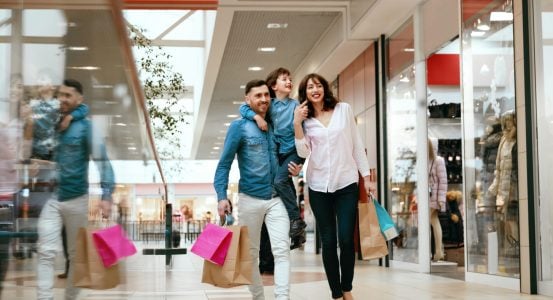 A happy family of three walking through a bright, modern shopping mall
