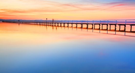 A long wooden pier stretching across a calm lake at sunset